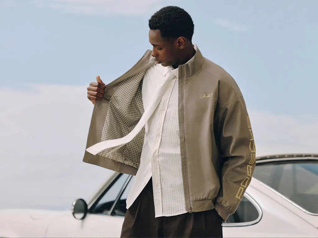 Person wearing jacket and shirt from the Pepita Collection – Porsche Legacy x PUMA in front of a Porsche 911.