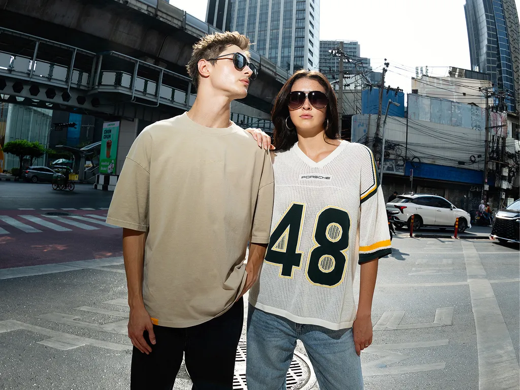 Two people wearing Porsche Design sunglasses and AHEAD collection on a city street with modern buildings.