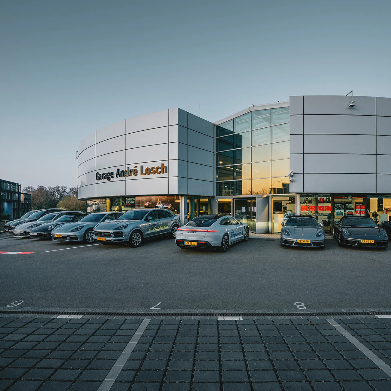 Porsche Zenter Lëtzebuerg vu de l'extérieur, avec plusieurs véhicules exposés devant le concessionnaire à Luxembourg.