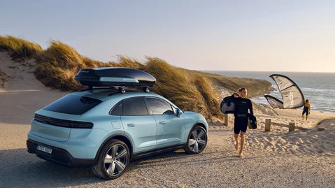 A man is walking on the beach next to a parked Porsche Macan 4 with a roof black box.