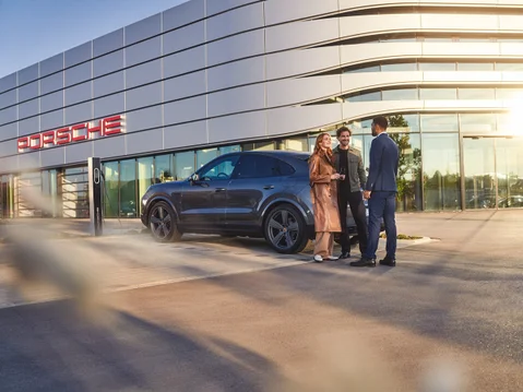 Osoby stojące na tle samochodu i salonu Porsche