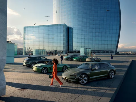 A woman walks past lined-up Porsche models of different colors.