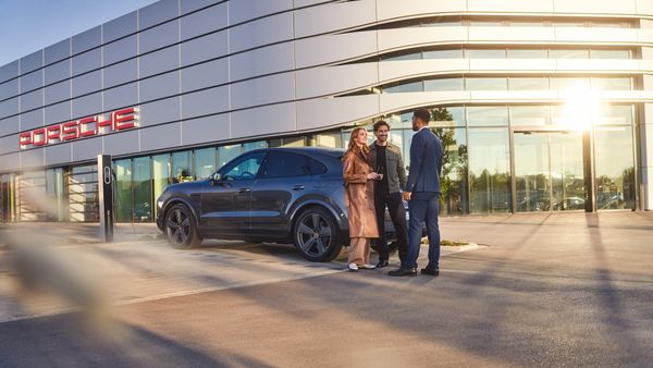 Osoby stojące na tle samochodu i salonu Porsche