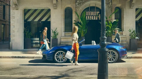 Una donna cammina vicino a un modello Porsche parcheggiato sulla strada di fronte a un grande edificio.