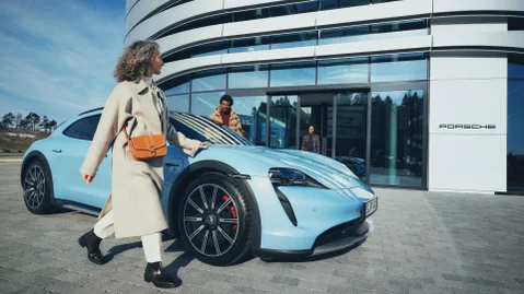 Customer arriving at a Porsche Centre, walking past a parked Porsche outside.