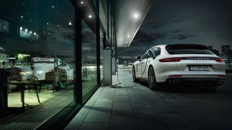 A white Porsche parked outside and charging next to a building.