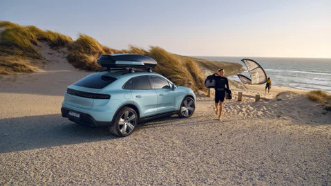 A man is walking on the beach next to a parked Porsche Macan 4 with a roof black box.