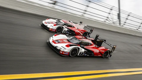 Two red and white Porsche 963 cars racing side by side in a circuit