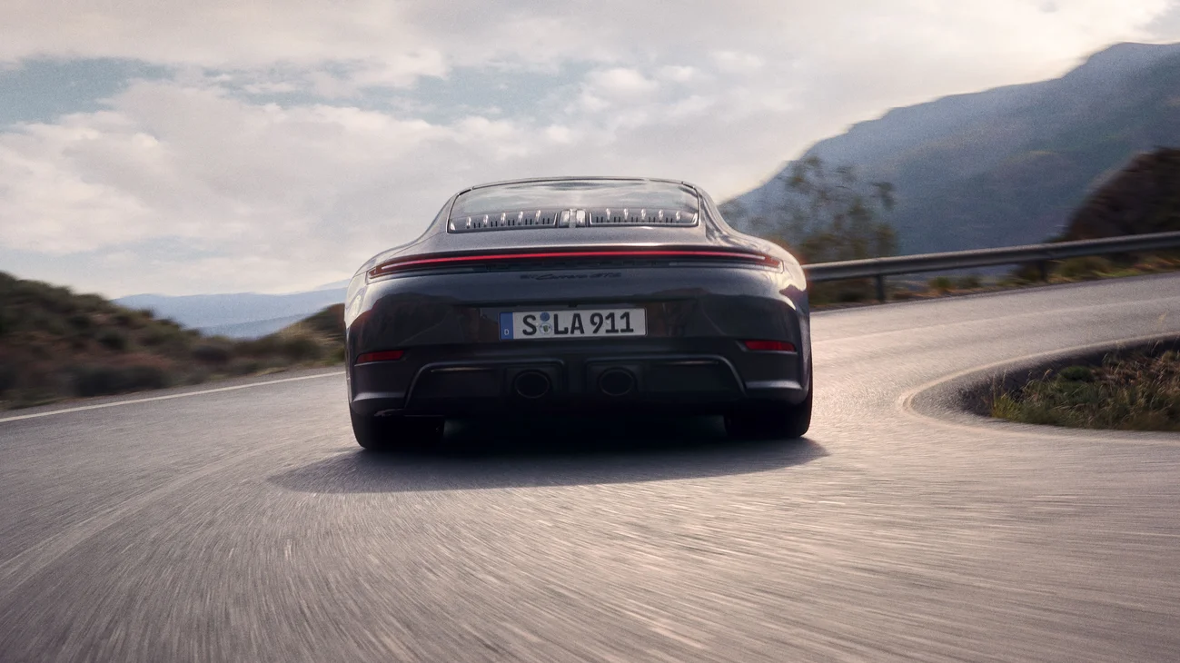 Rear shot of  a Slate Grey Neo colored 911 Carrera GTS driving on a street in the mountains.
