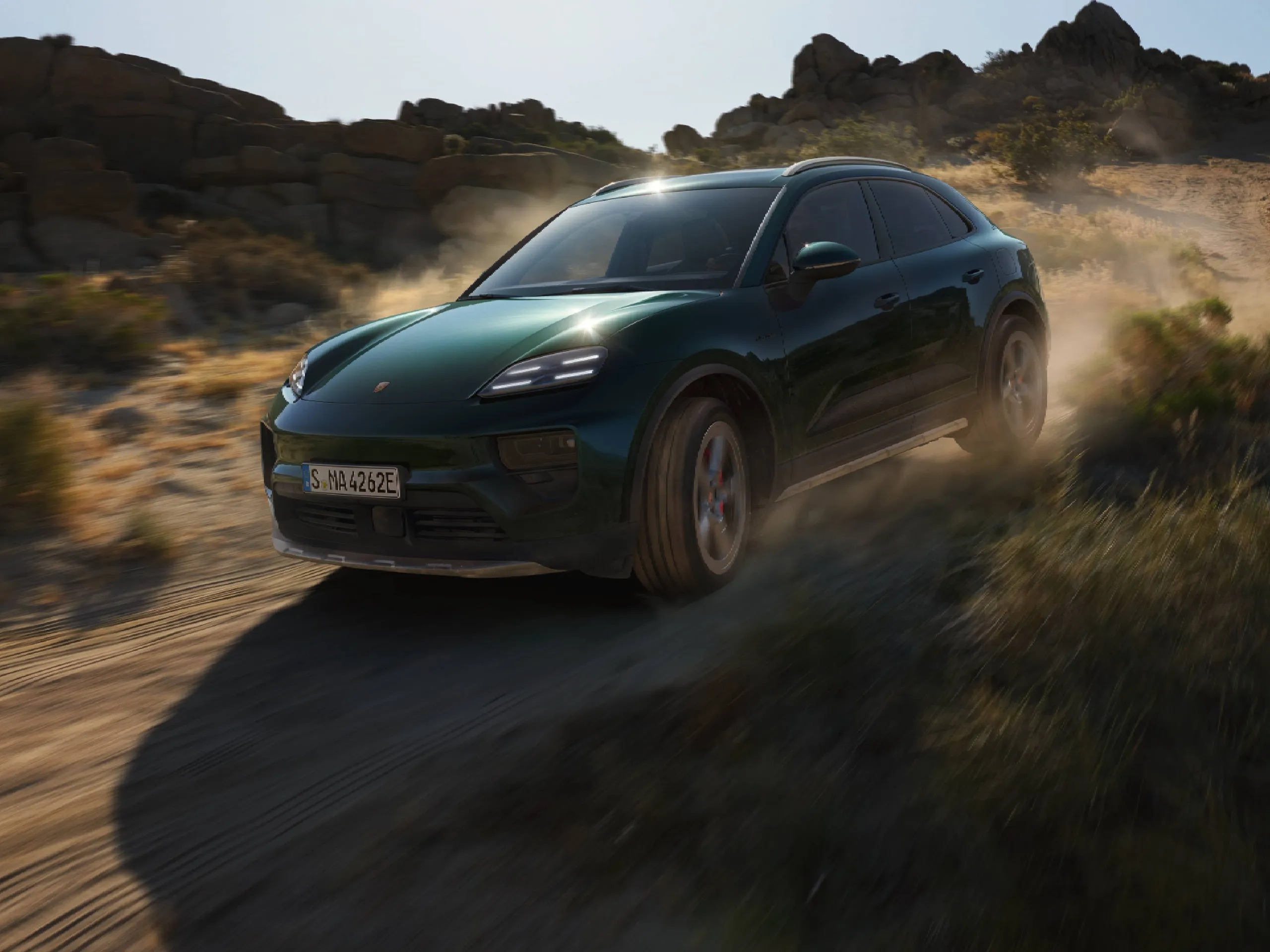 An Oak Green Metallic Neo Macan 4S driving through a barren, rocky landscape.