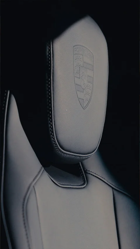 Close up of a car seat with a Porsche crest on the headrest.